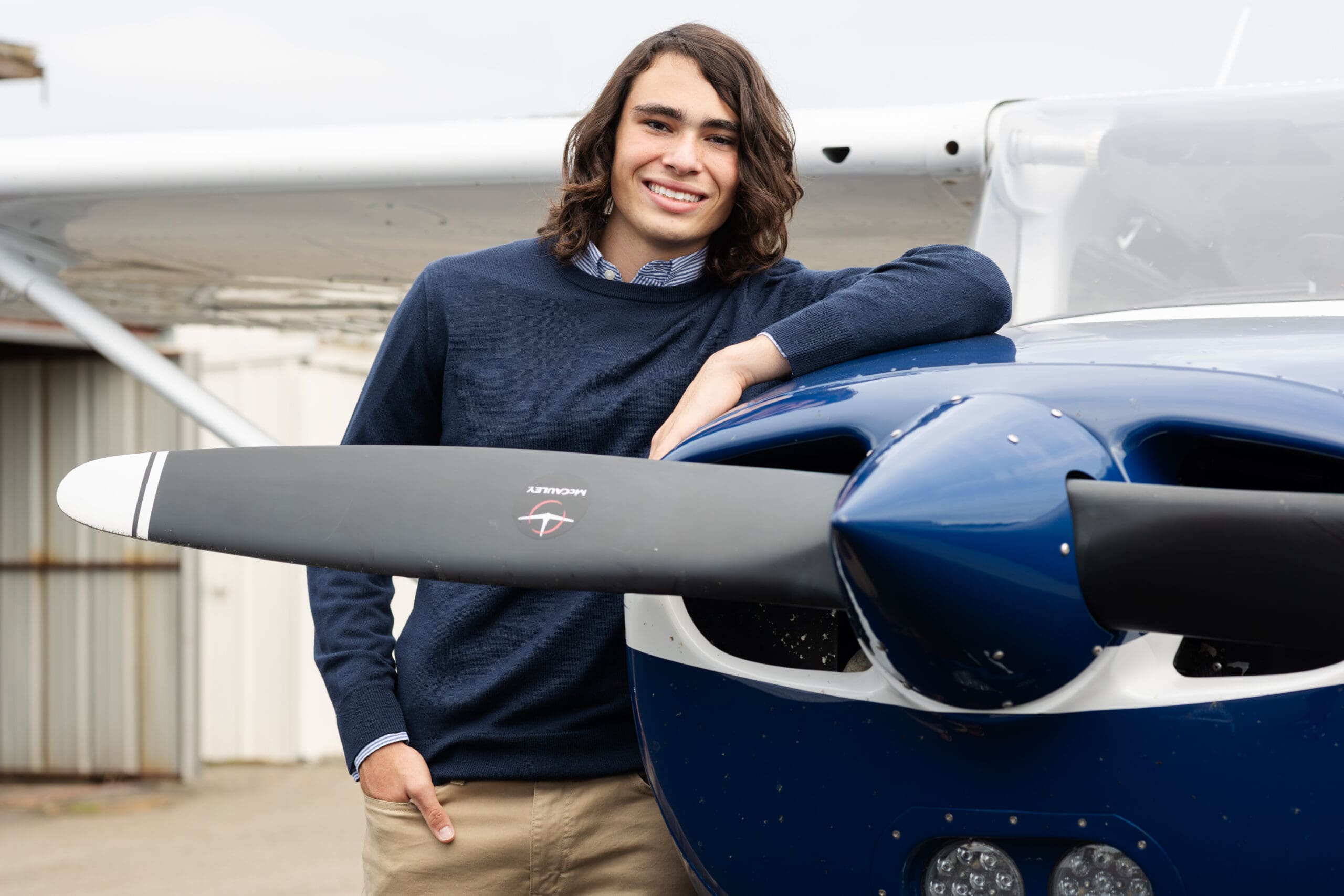 High school senior boy standing beside small airplane at Morristown Airport in Morris County NJ